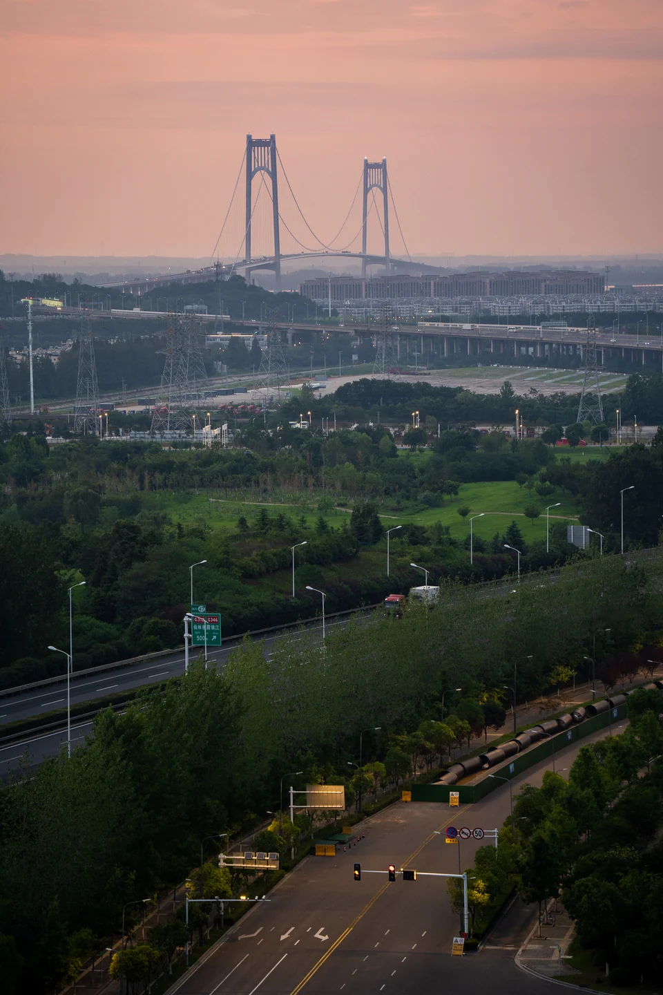 A distant suspension bridge rises above a tree-lined river at dusk.