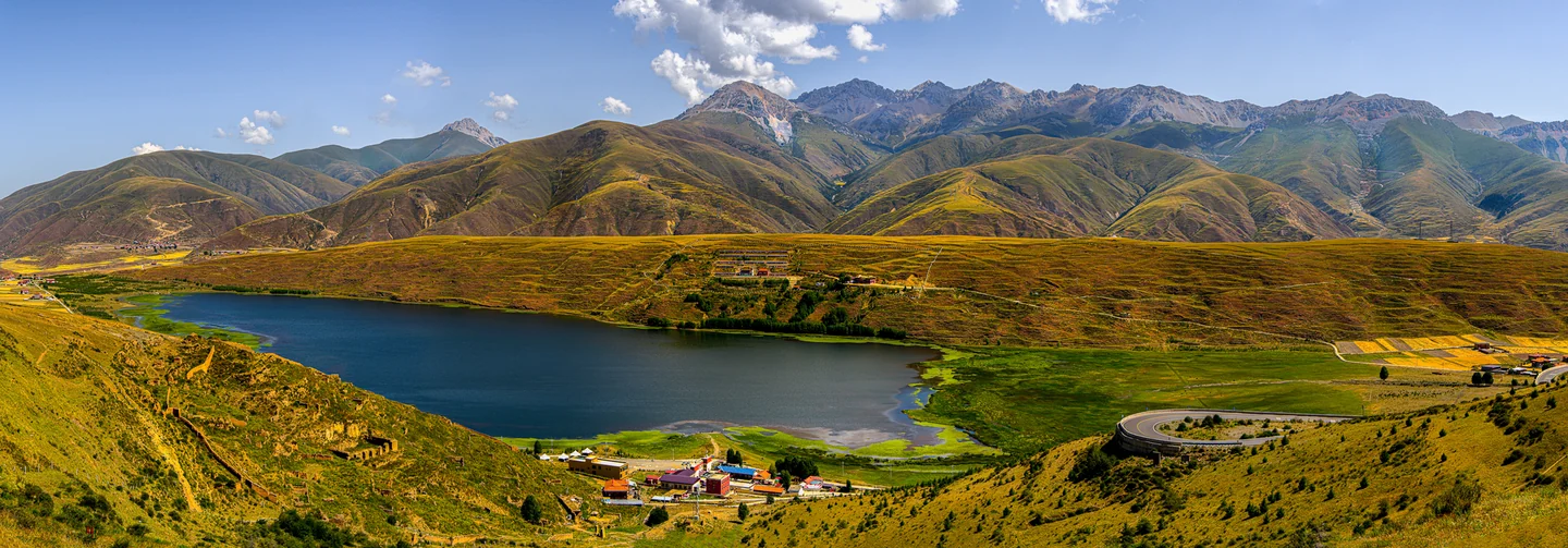 A blue lake curves through golden grassland below a long mountain ridge.