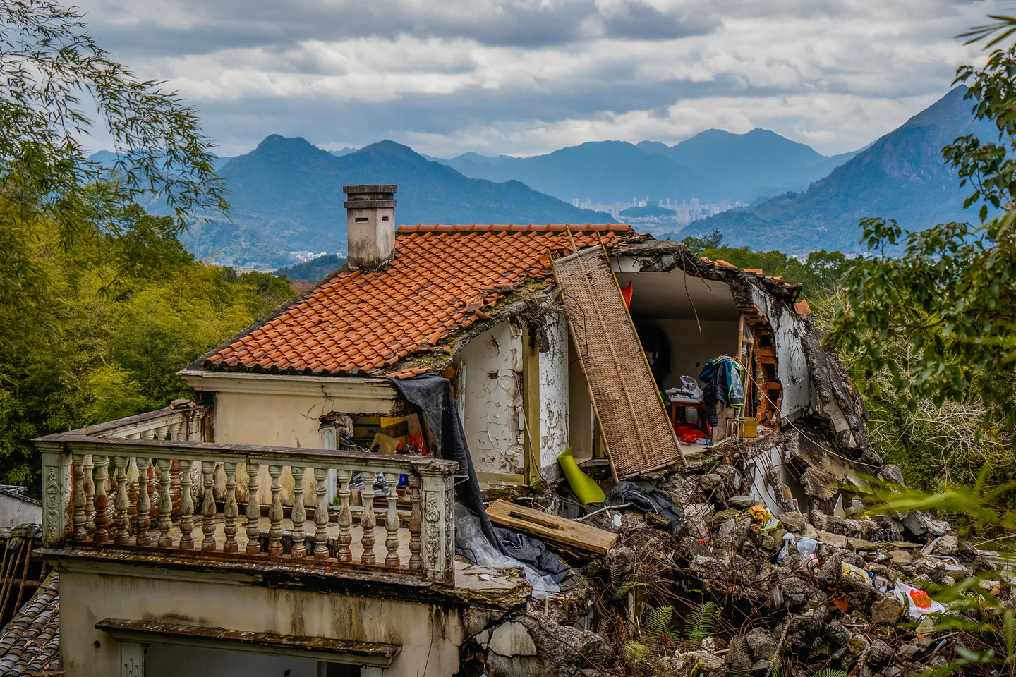 An old red-roofed house sits among green hills beneath a cloudy mountain sky.