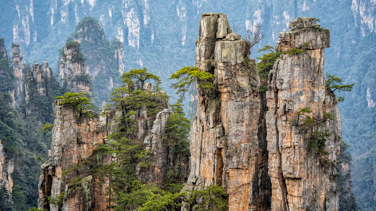 Tall weathered stone pillars dotted with green trees stand before distant cliffs.